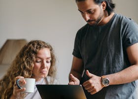 Young couple using a laptop while unpacking in a new home, planning their move online.