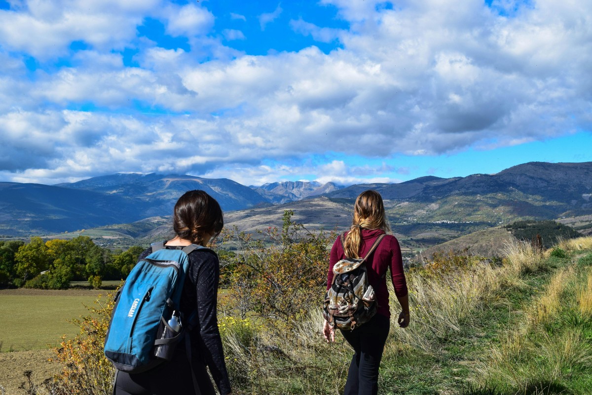 Two women hiking on a mountain trail with scenic views under a blue sky.