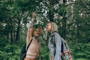 Two women happily exploring a beautiful green forest, enjoying nature and adventure.
