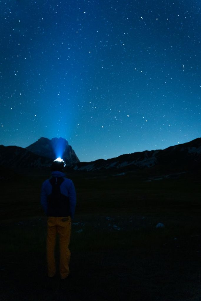 A person stands under a starry night sky using a flashlight, embracing adventure and nature.