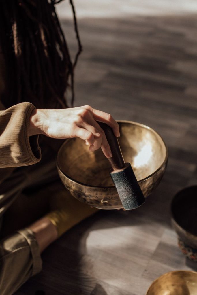 Hand holding a mallet over a Tibetan singing bowl for meditation practice.