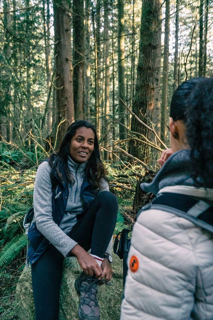 Two women hikers enjoy a winter hike, sitting and talking in a lush forest.