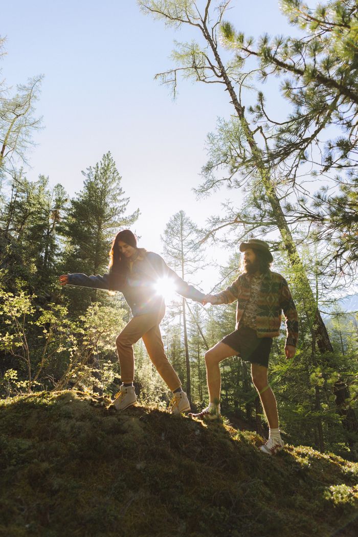 A couple hikes on a forest trail with sunlight streaming through trees.