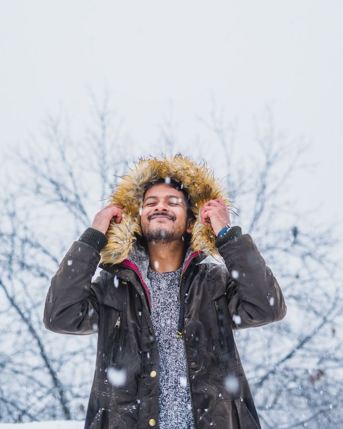 Smiling man in a fur hooded jacket relishing the winter snowfall outdoors.