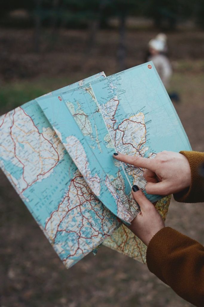 A woman holds a map while navigating through an outdoor park trail, pointing at a location.