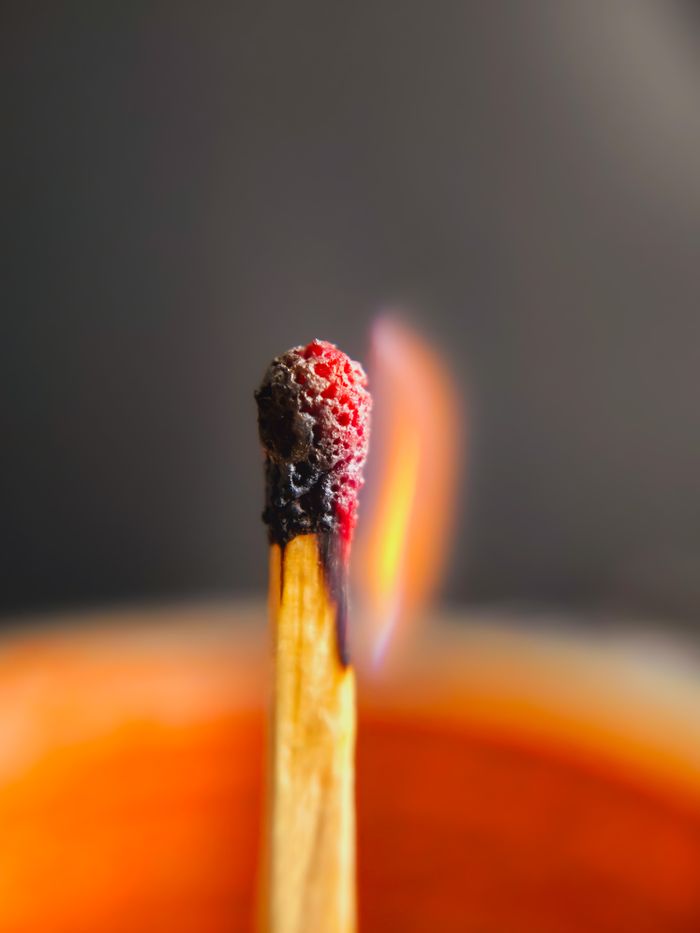 Detailed macro shot of a matchstick burning with soft flame against blurred background.