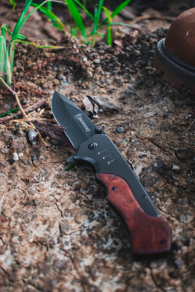 Close-up of a folding pocket knife with wooden handle on rustic ground.